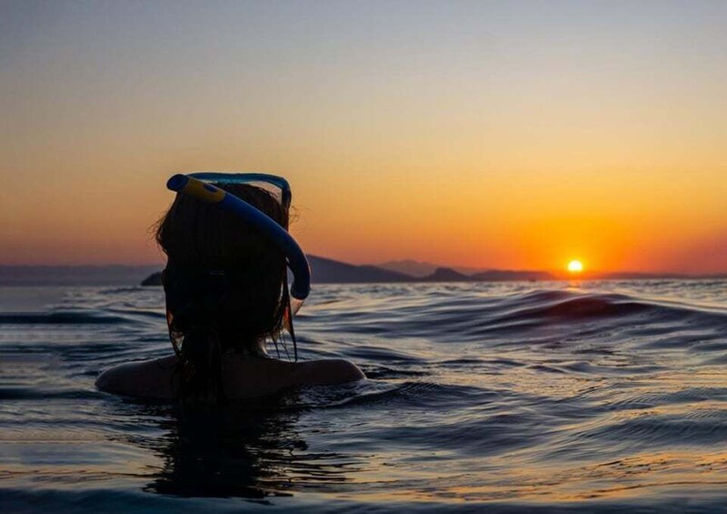 A person in the water at sunset with the sun visible on the horizon. 1