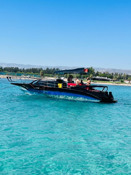 A boat with passengers on a clear day, surrounded by calm turquoise waters and a distant shoreline. 1