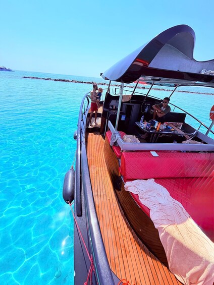 A boat with a wooden deck, a red cushioned area, and a person holding a child. 2