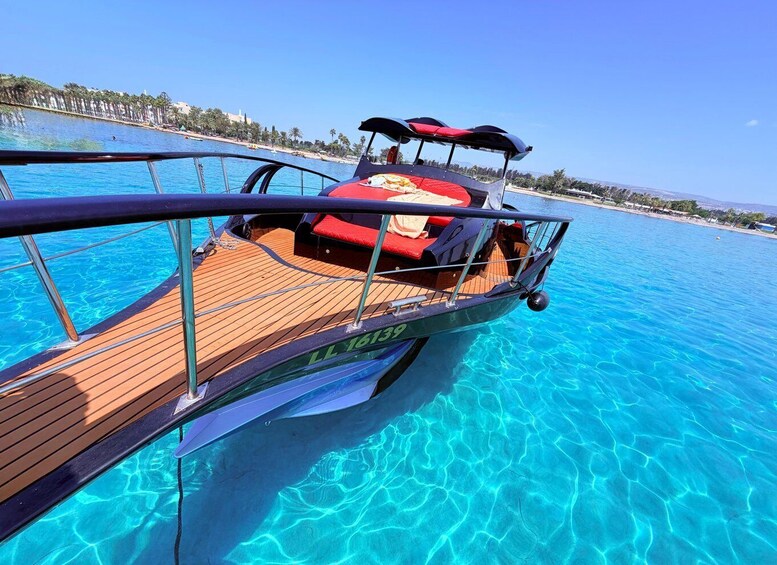 A boat with a wooden deck and a red cushion on the bow, floating on clear blue water. 3