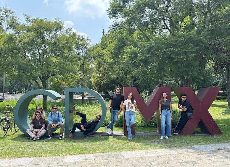 A group of people posing in front of large metallic letters spelling 'GOMIX' in a park with trees and a paved path. 5