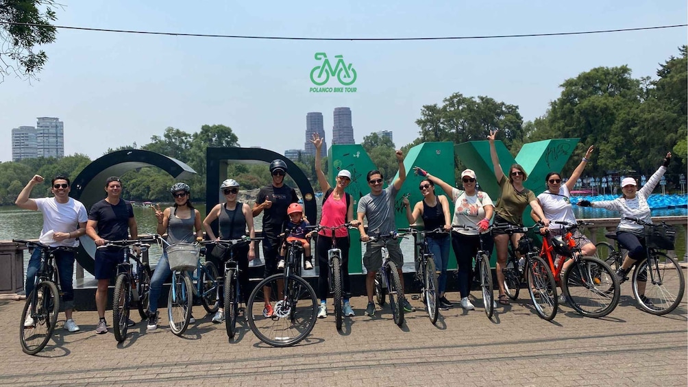 A group of people on bicycles in front of a large green sign with the letters 'GOD' and a logo above it. 3