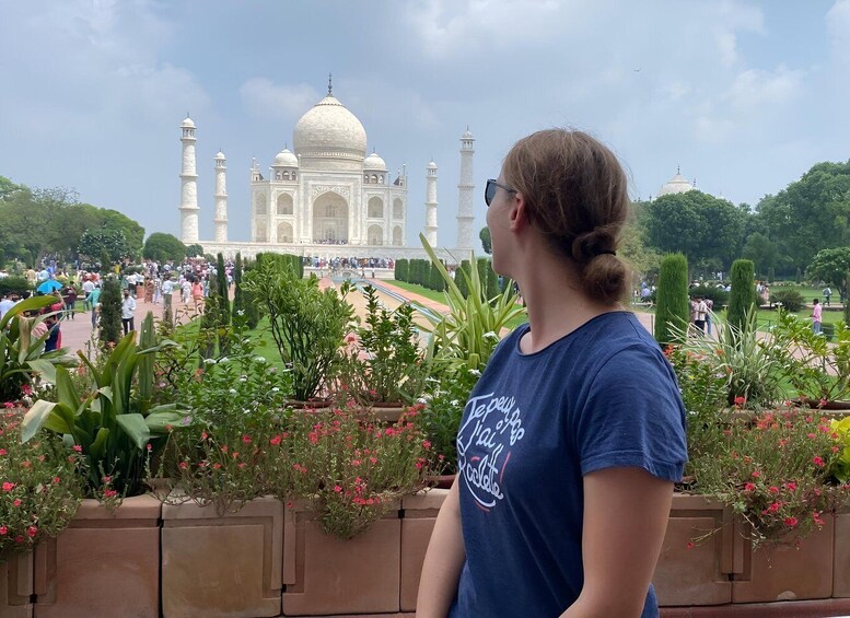 A person standing in a garden with the Taj Mahal in the background. 1