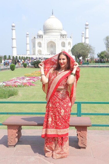 A person in traditional attire standing in front of the Taj Mahal with a garden and visitors in the background. 3