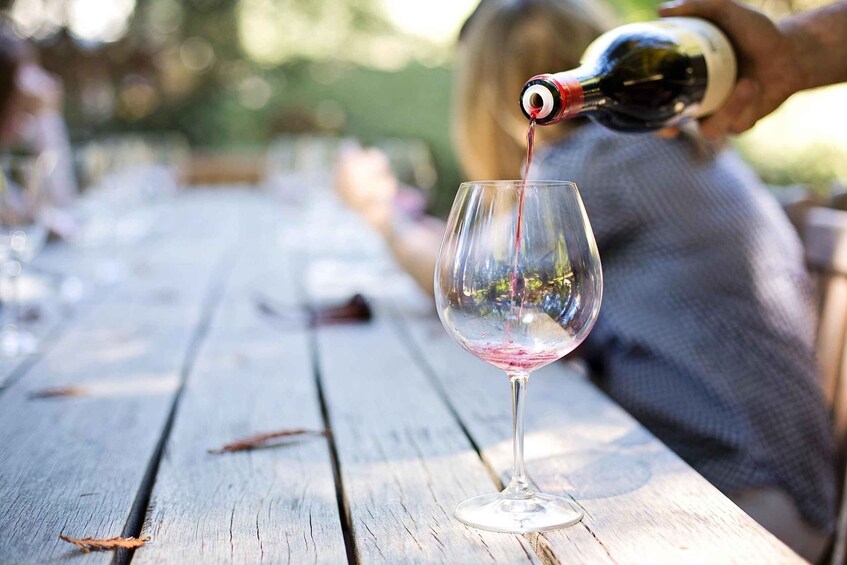 A wine bottle pouring red wine into a glass on a wooden table. 3