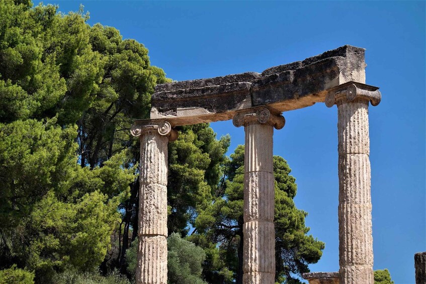 Ancient stone columns with a broken top, surrounded by lush green trees. 1