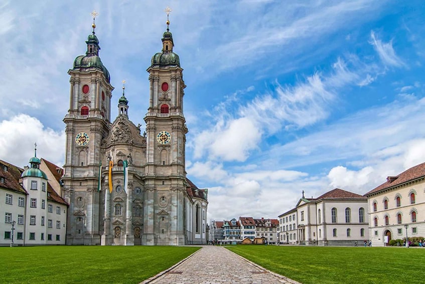 A historic church with two prominent towers, a cobblestone pathway, and surrounding classical architecture. 2