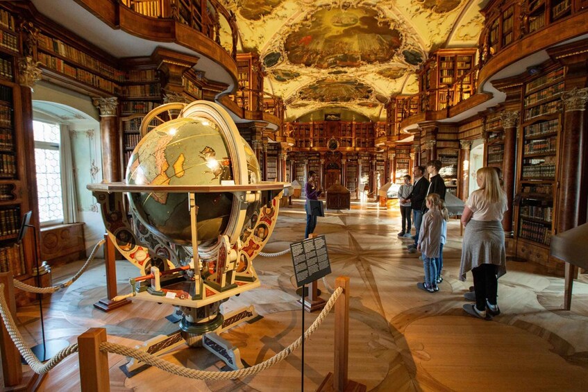 A grand library interior with ornate woodwork, a large globe, and visitors. 3