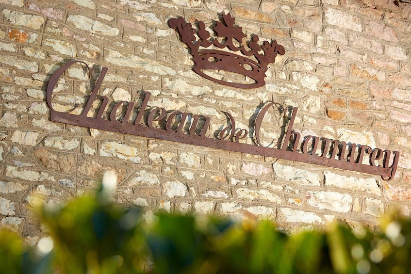 A metal sign with 'Chateau de Chambrey' and a crown symbol on a brick wall. 2