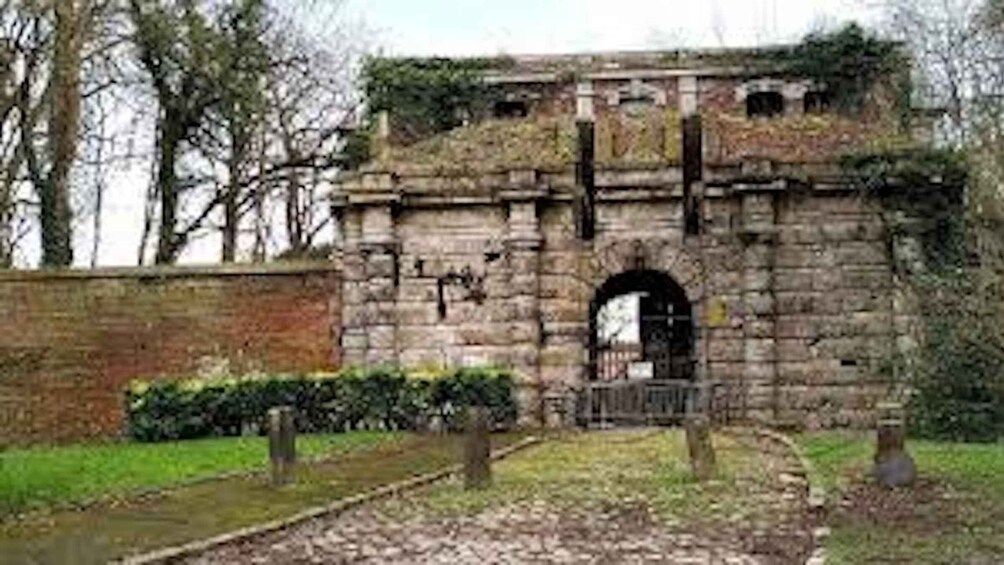A stone structure with a central archway, surrounded by greenery and a brick wall. 4