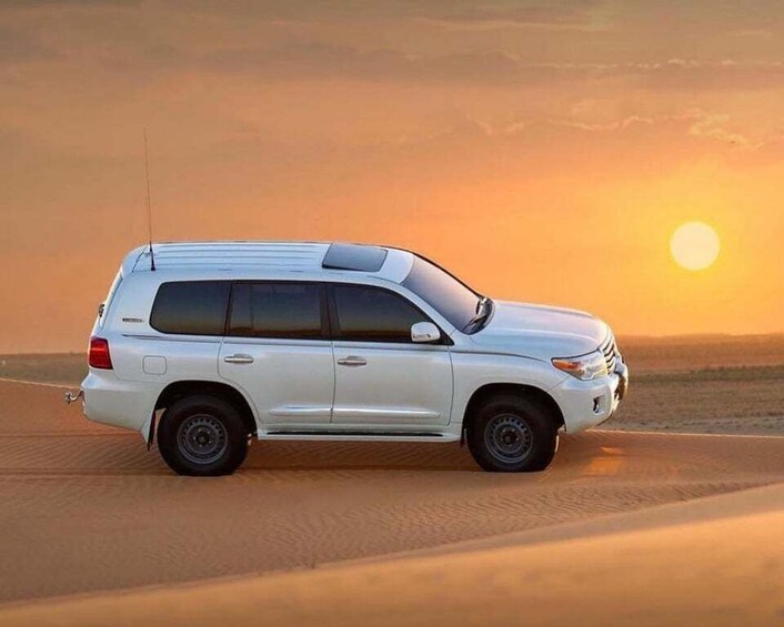 A white SUV parked on a desert dune at sunset. 2