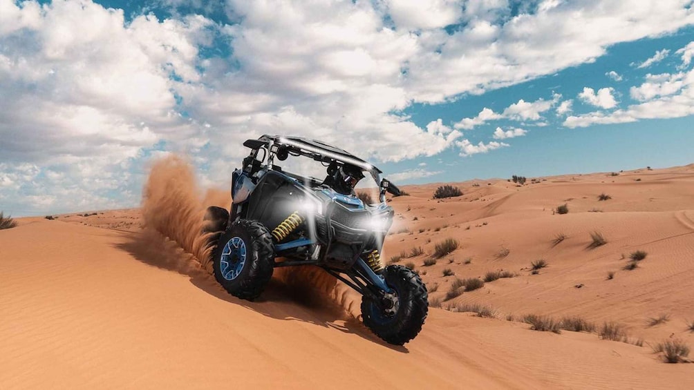 A quad bike driving through a desert with sand dunes and a partly cloudy sky. 4
