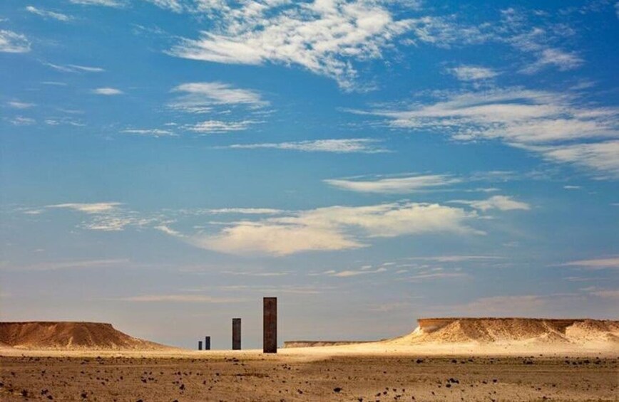 A desert landscape with three tall, narrow structures in the distance. 1