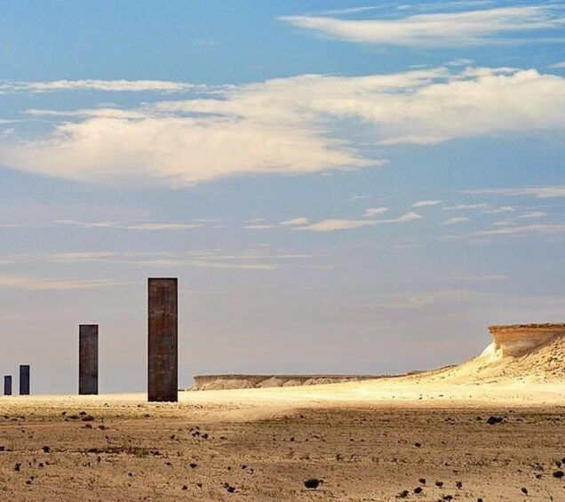 A desert landscape with three tall, rectangular structures and a large sand dune in the background. 4