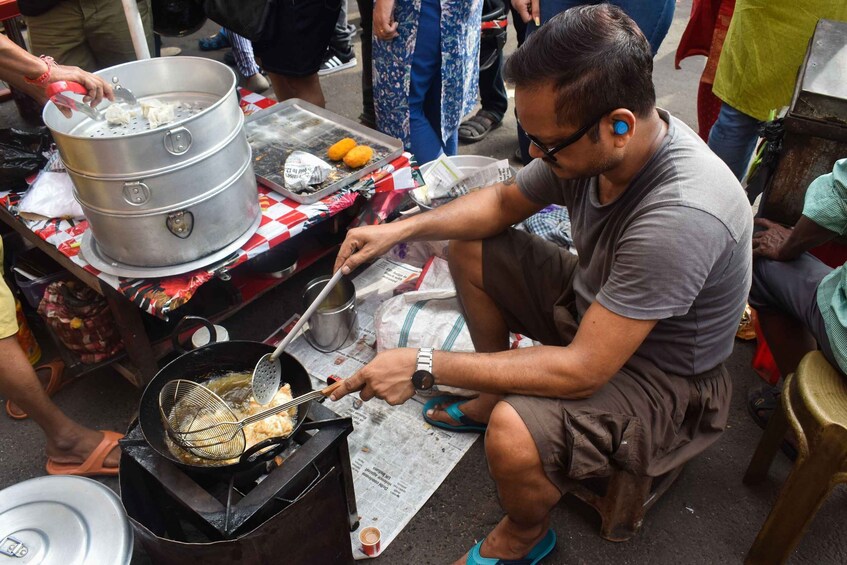 A person cooking at an outdoor food stall, using a large pot and a frying pan. 3