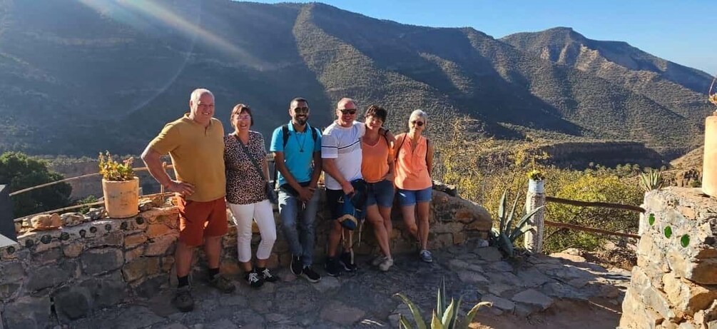 A group of people standing on a stone wall with a mountainous landscape in the background. 5