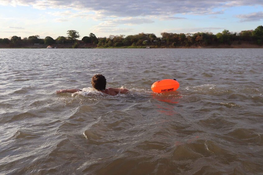 A person swimming in a body of water with an orange flotation device. 3