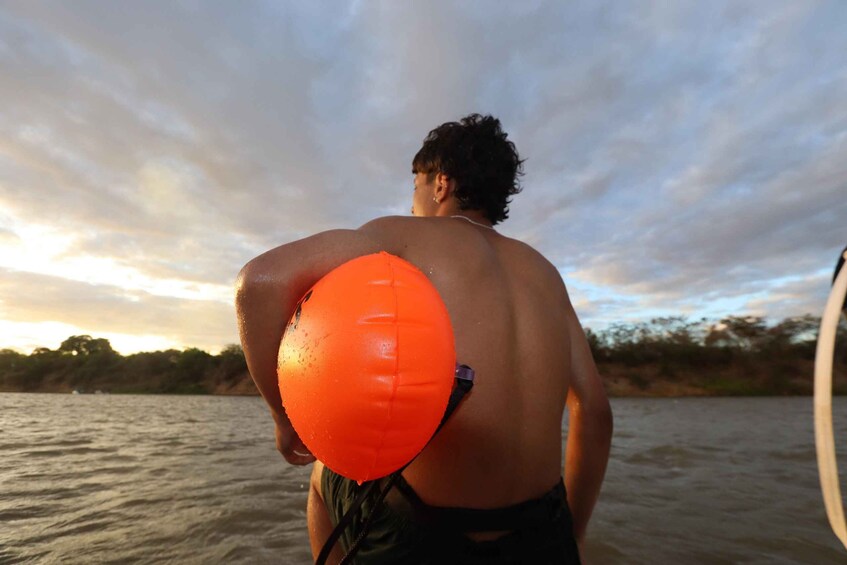 A person holding an orange object, standing by a body of water with a cloudy sky. 1