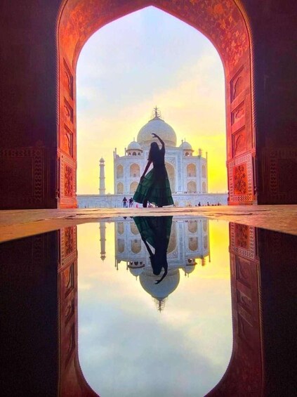 A person in a green dress standing in front of the Taj Mahal, with a reflection visible in the water. 5