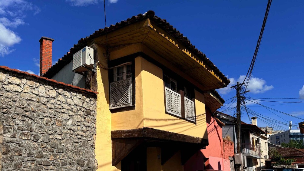 A yellow building with a stone wall, a red roof, and a chimney. 1