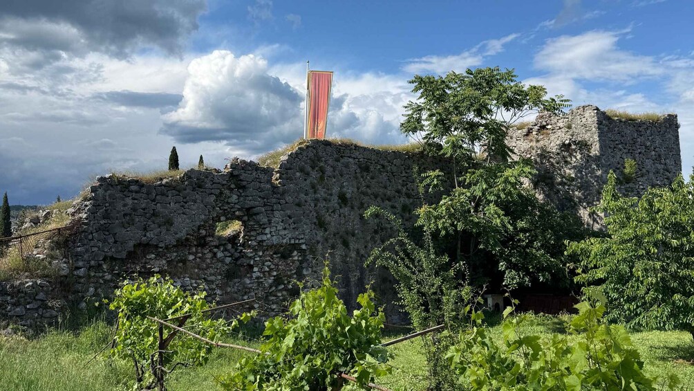 A stone ruin with a flag on top, surrounded by greenery and a clear sky. 3