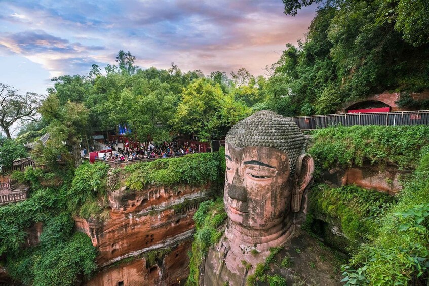 A large Buddha statue surrounded by lush greenery and a crowd of visitors. 1