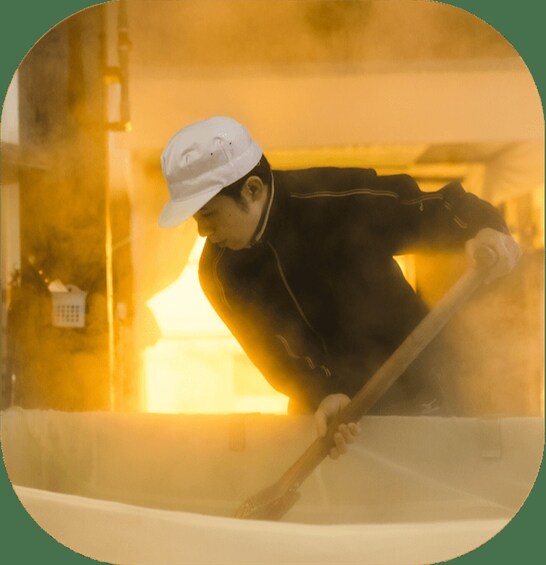 A person in a white hard hat and dark clothing, working with a tool in a yellow-lit environment. 2