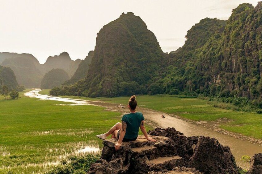 A person sitting on a rock by a river in a mountainous area. 2