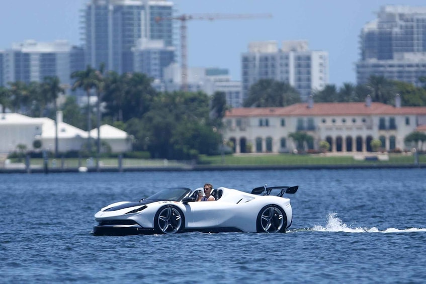 Un'auto sportiva bianca sfreccia attraverso l'acqua sullo sfondo di uno skyline cittadino. 1
