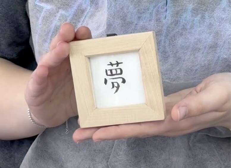 A person holding a small wooden frame with a white background and black text. 3