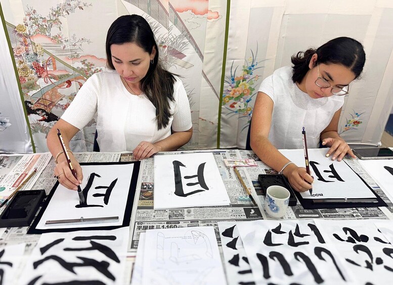 Two individuals practicing calligraphy on paper with ink brushes, surrounded by newspapers and ink pots. 4
