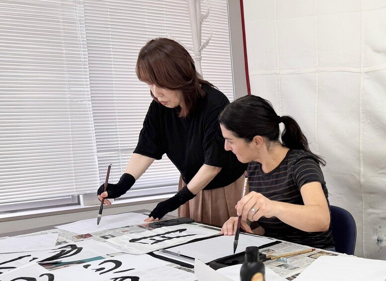 Two people engaged in a calligraphy activity, with papers and calligraphy tools on a table. 3