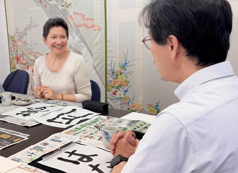 Two people sitting at a table with newspapers and a cup. 5