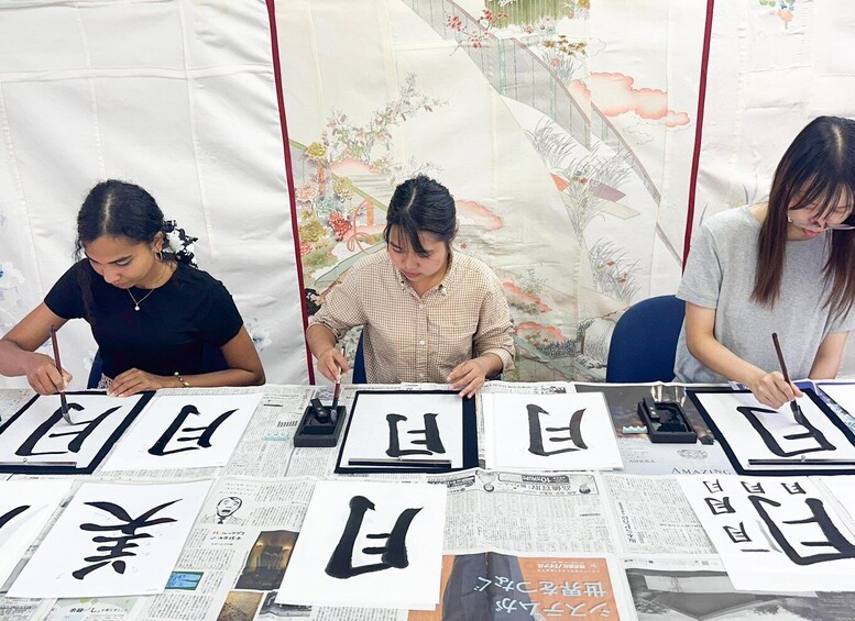 Three people practicing calligraphy at a table with papers and brushes. 2