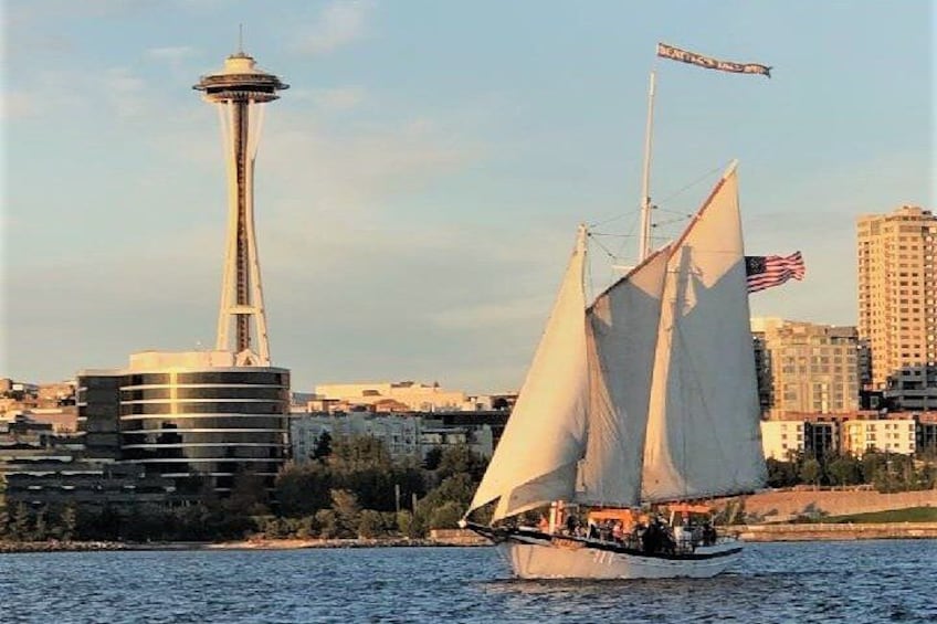 A sailboat with white sails on water, a tall tower, and a cityscape with buildings and a bridge. 1