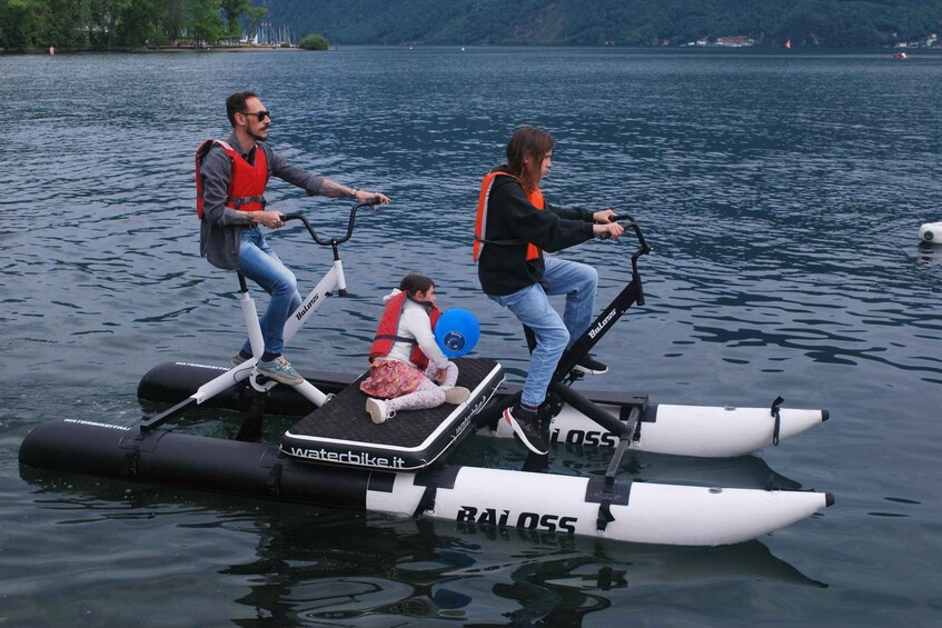 Two people riding a water bike with a child on a platform, on a calm lake with distant hills. 4