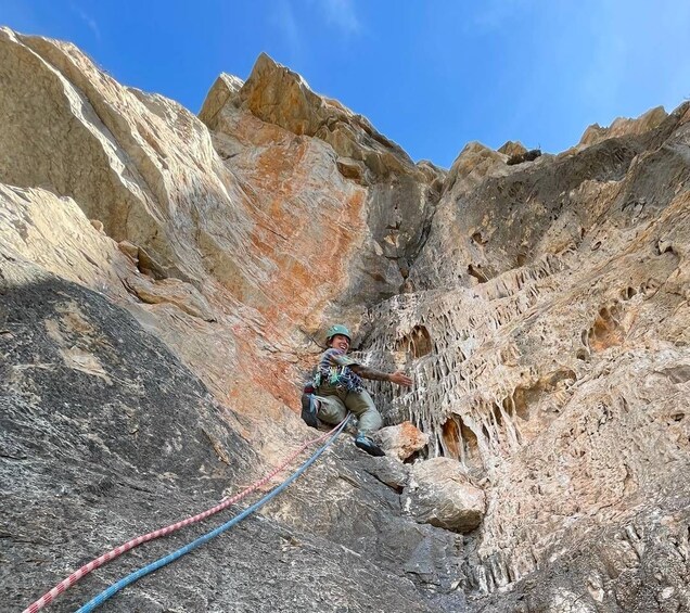 A person rock climbing in a rocky canyon with visible crevices and a clear blue sky. 1