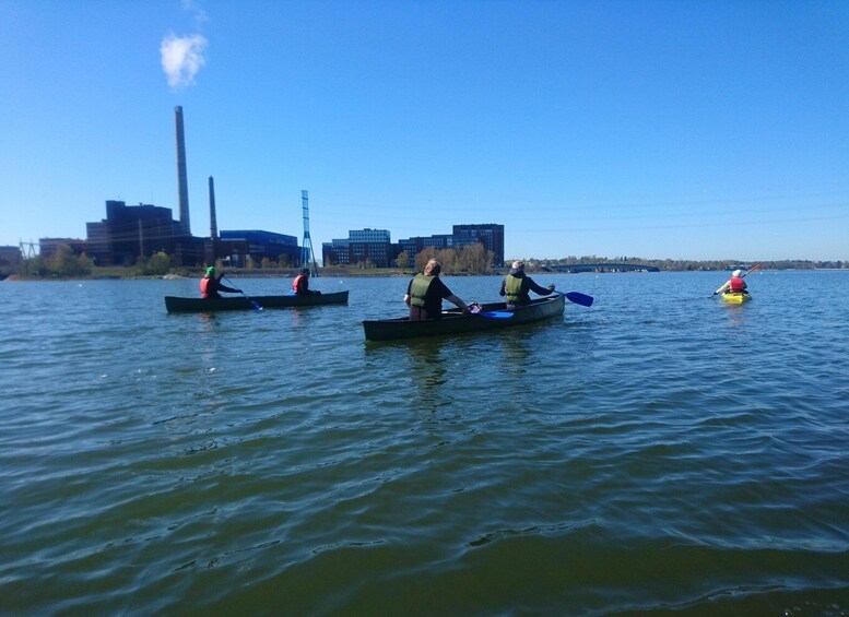 Three kayaks on a calm body of water with industrial buildings in the background. 3