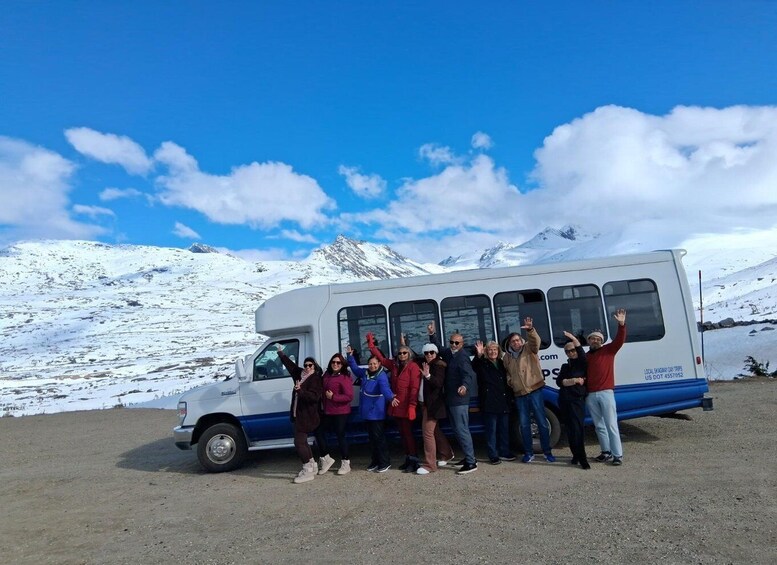A group of people posing in front of a bus with a snowy mountain landscape in the background. 4