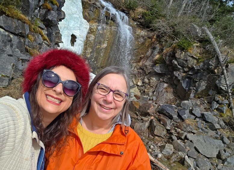 Two people standing in front of a waterfall with rocky terrain and sparse vegetation. 5