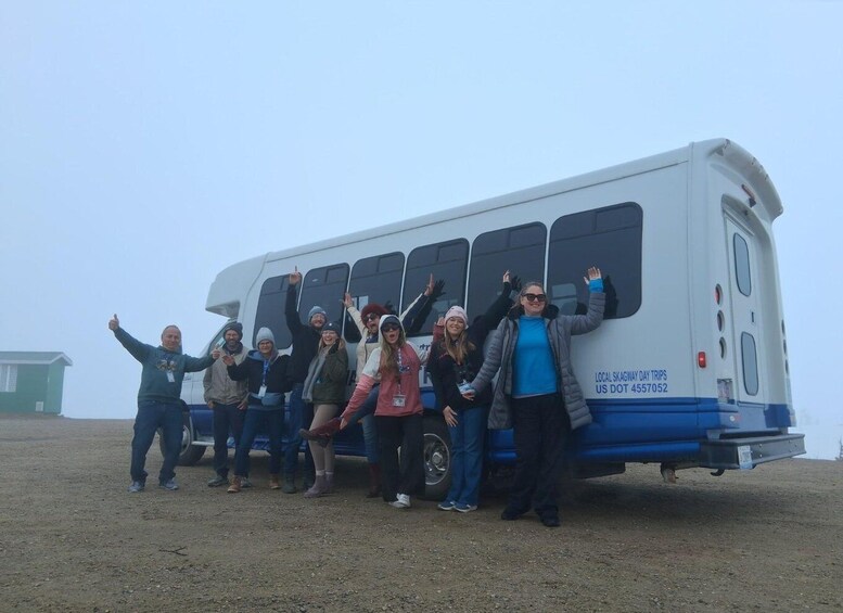 A group of people posing in front of a bus with the text 'LOCAL SKAGWAY DAY TRIPS US DOT 4557052' on its side. 2