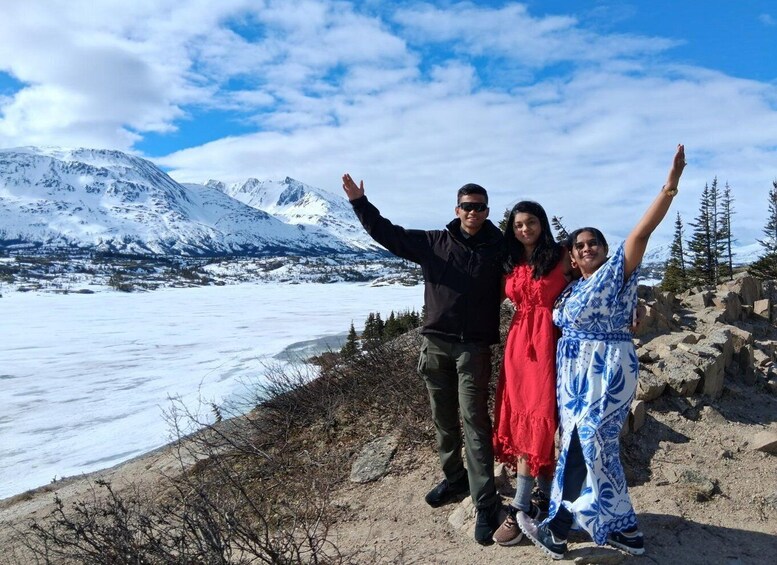 A group of people standing on a rocky shore with a snowy mountain range in the background. 5