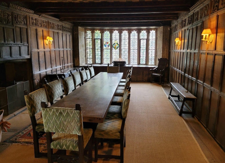 A long wooden table with upholstered chairs, surrounded by wooden paneling and stained glass windows. 2