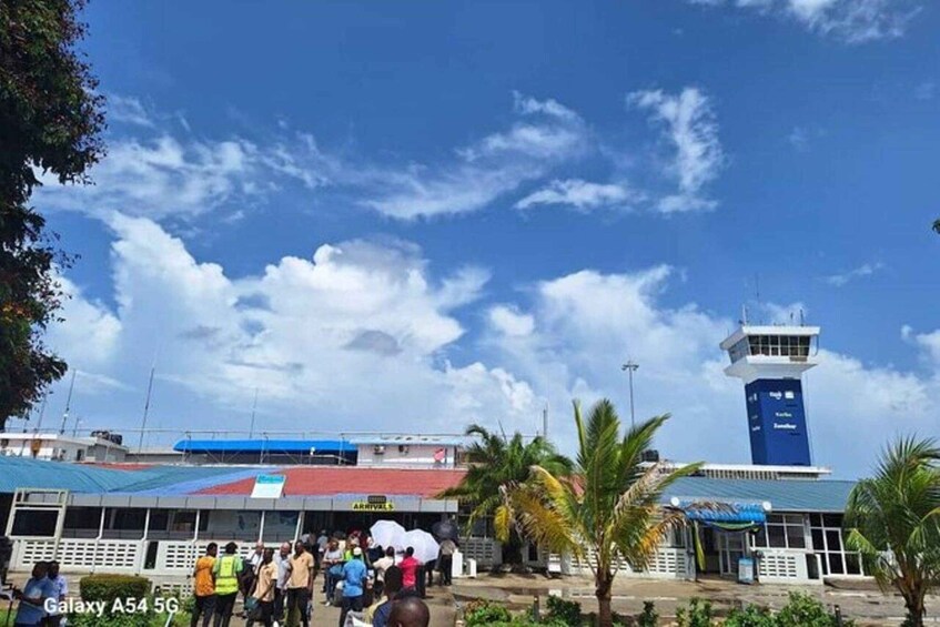 An airport terminal with a control tower, palm trees, and a clear sky. 2
