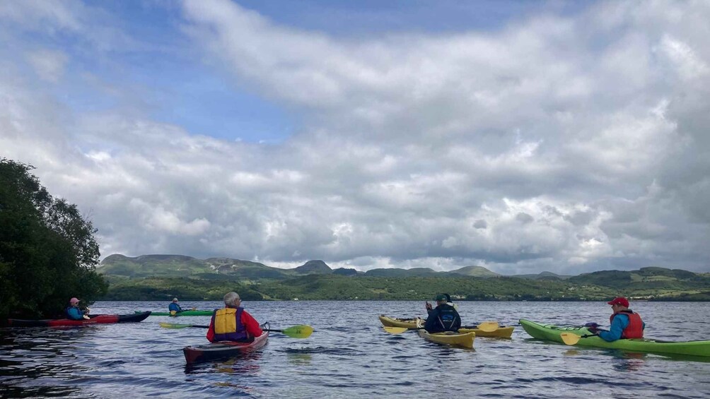 A group of kayakers on a calm lake with a cloudy sky and green hills in the background. 2