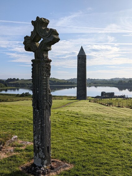 A stone pillar with a cross, a tall tower, and a lake in the background. 1