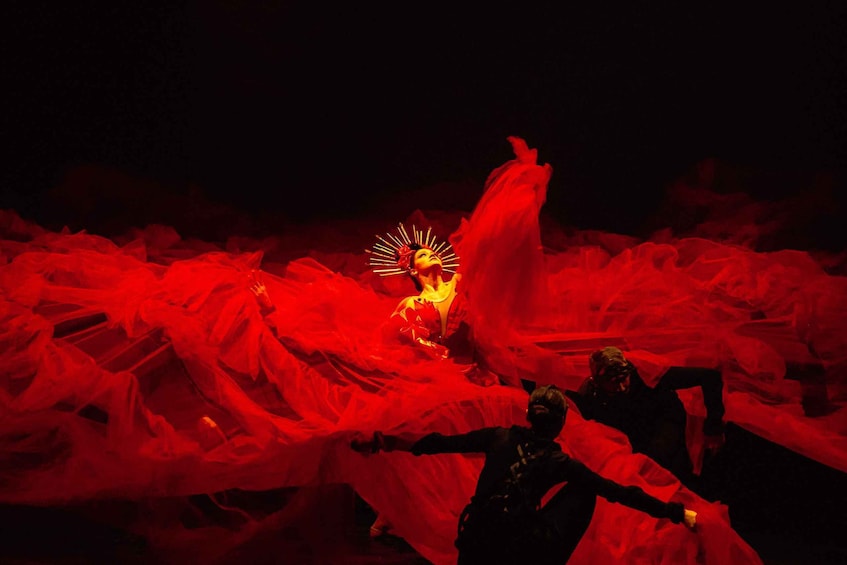 A person in a red dress with a halo, surrounded by red fabric. 5