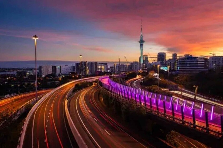 A cityscape at dusk with a prominent tower, curved highways, and purple-lit barriers. 4