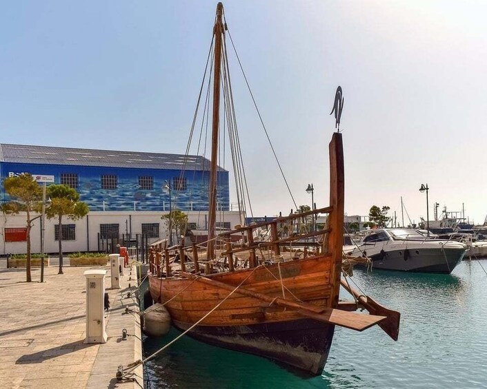 A wooden boat docked at a marina with a modern building in the background. 3