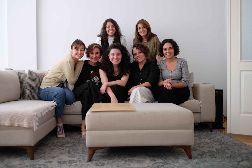 A group of people sitting on a couch in a living room with a patterned rug and a white door in the background. 5